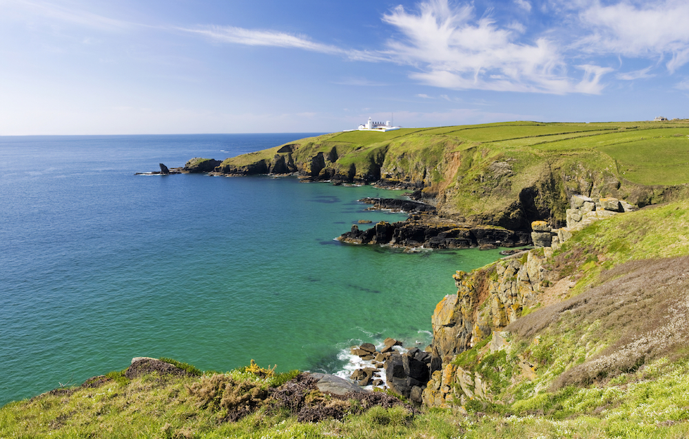 The coastline and the Lizard Point (with its lighthouse) in Cornwall, England on a spring day. View from the Southwest Coastal footpath over Housel Bay